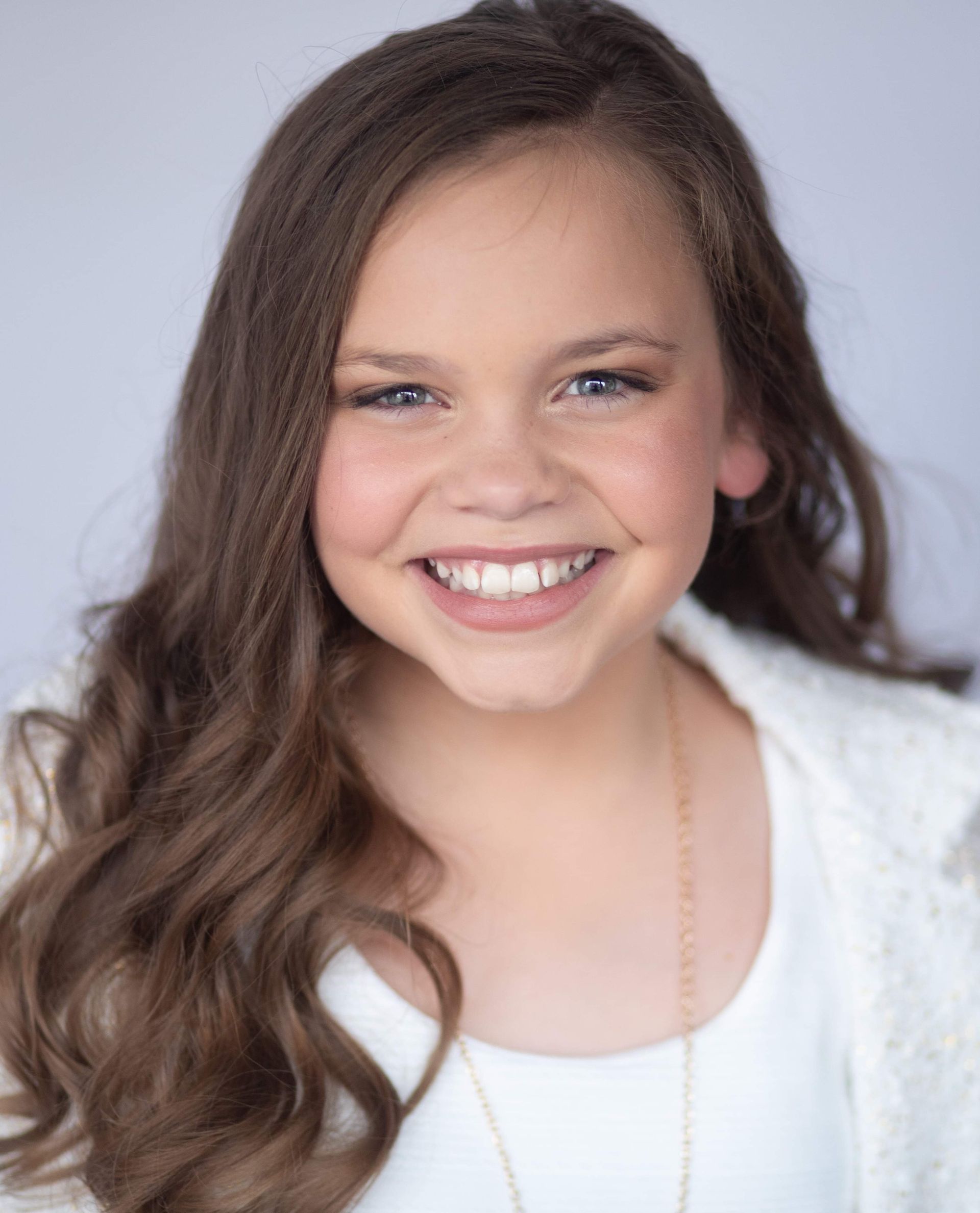 A young girl with long brown hair is smiling for the camera.