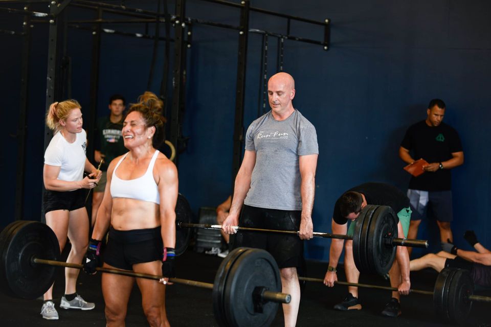 A man in a blue shirt is lifting a barbell in a gym.
