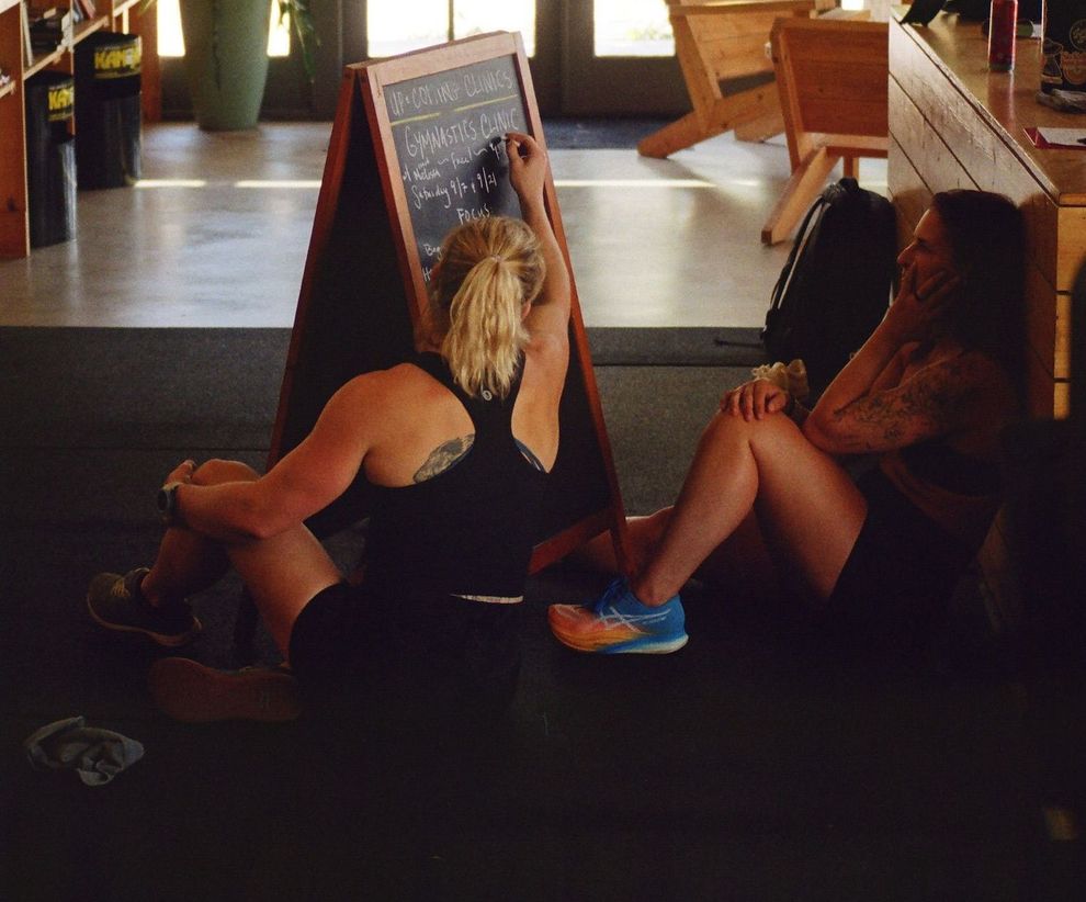 Two women sit on the floor writing on a chalkboard