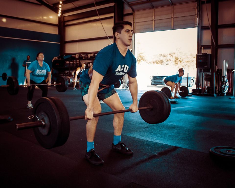 A man in a blue shirt is lifting a barbell in a gym.