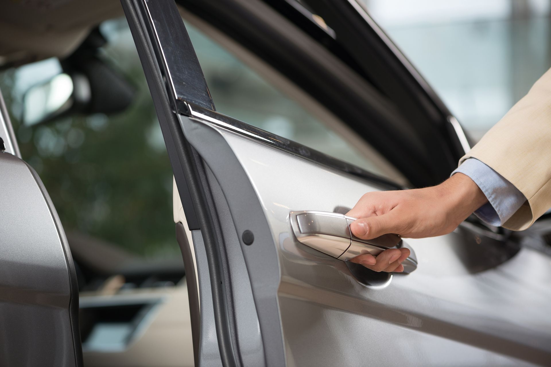 Persona che apre la portiera di un'auto; auto argentata, giacca beige, all'aperto.
