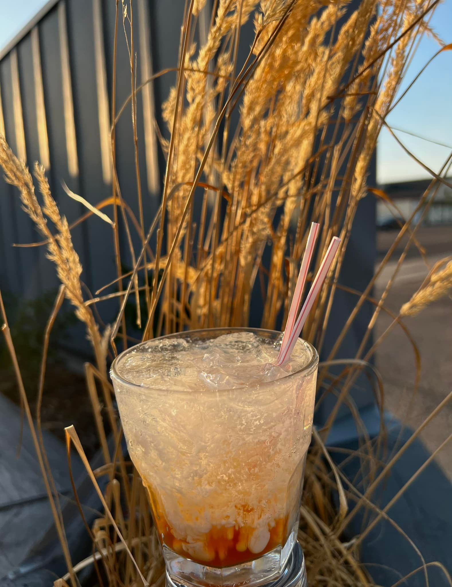 A drink with a straw in it is sitting in front of tall grass.