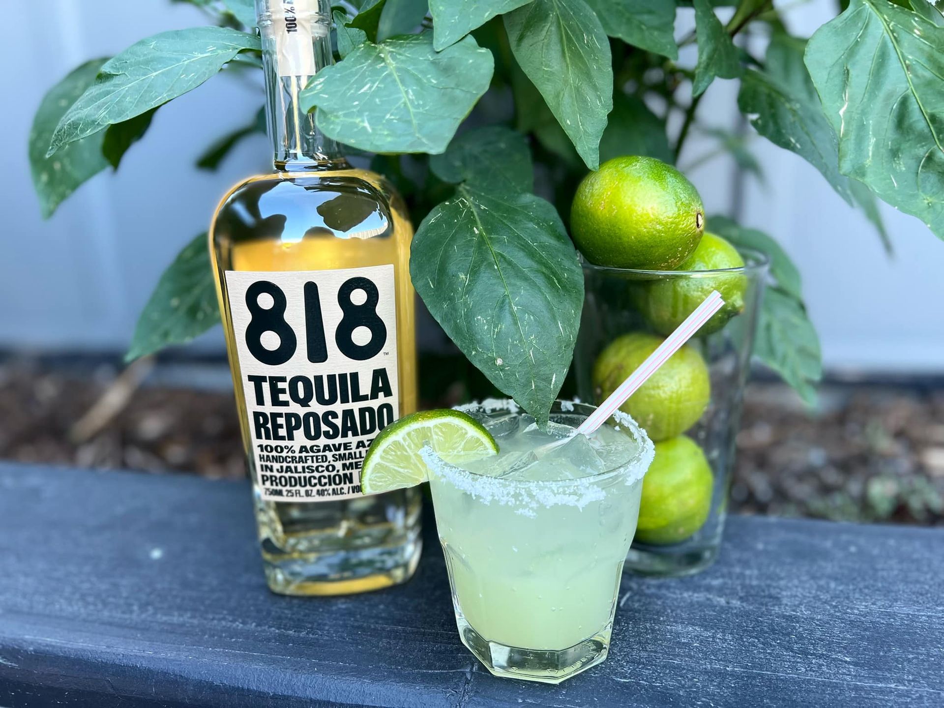 A bottle of 818 tequila reposado next to a glass of margarita.