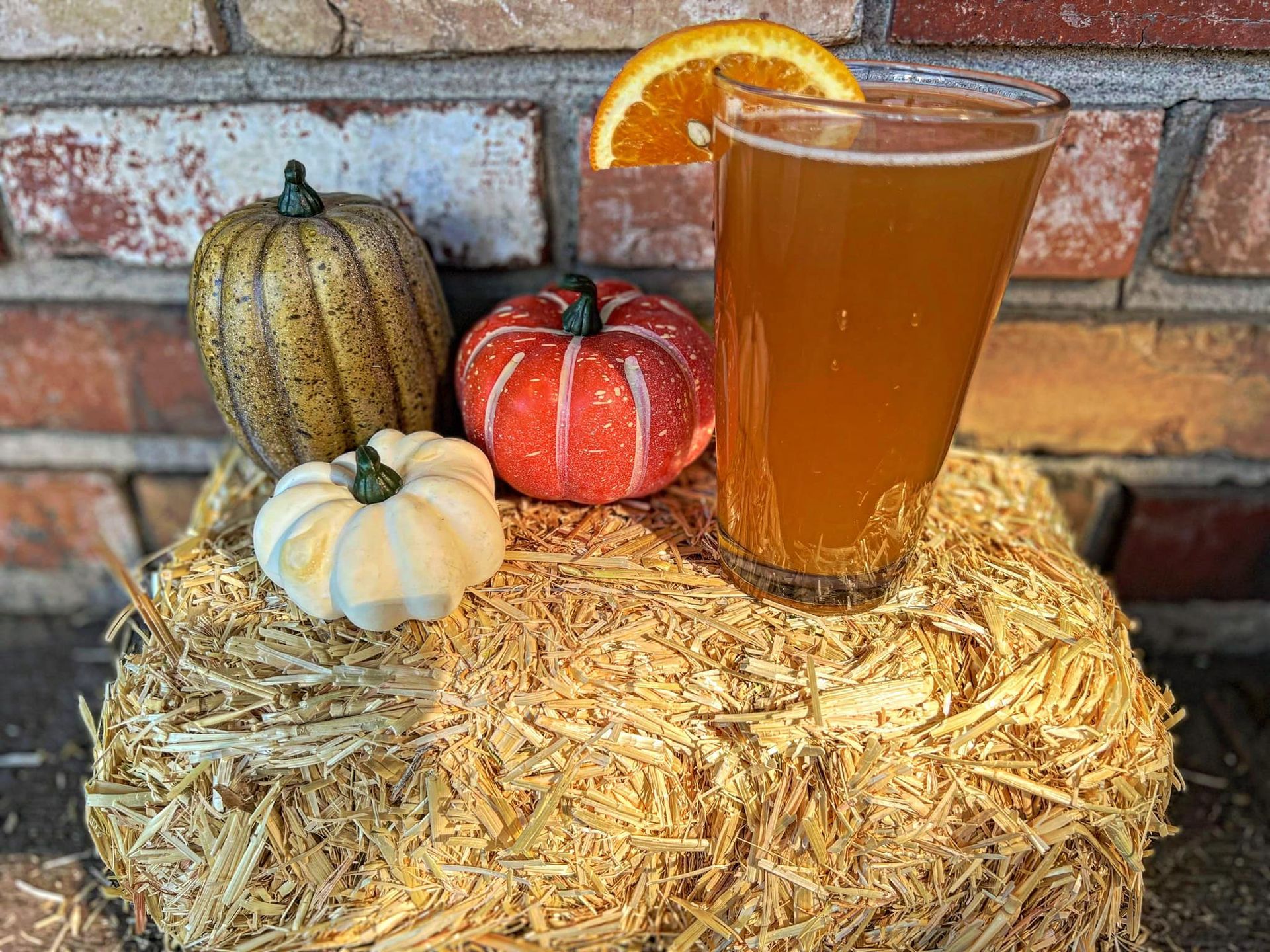 A glass of beer is sitting on top of a bale of hay next to pumpkins.