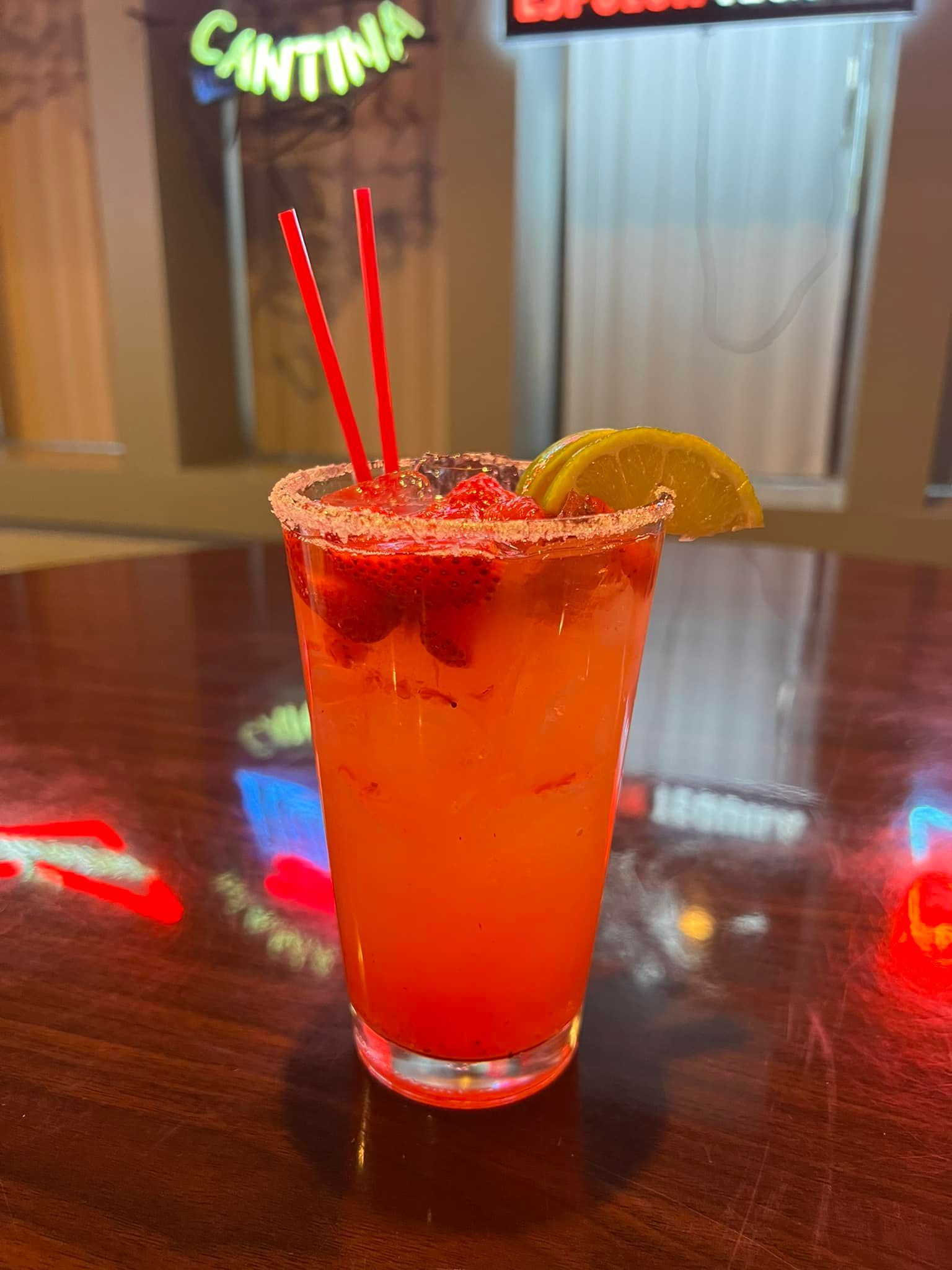 A glass of orange liquid with strawberries and a lime on a table.
