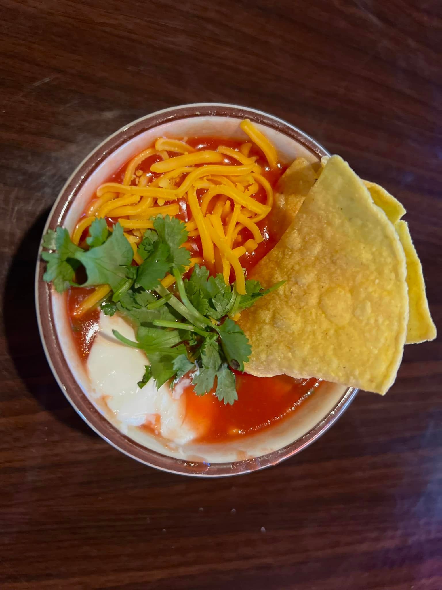 A bowl of chili with cheese , sour cream and tortilla chips on a wooden table.