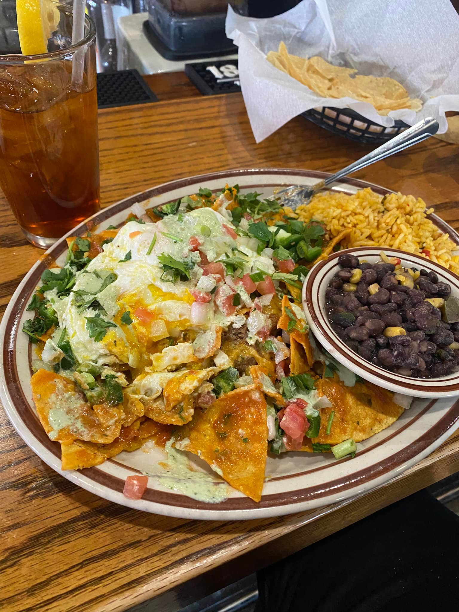 A plate of nachos , rice and beans on a wooden table.