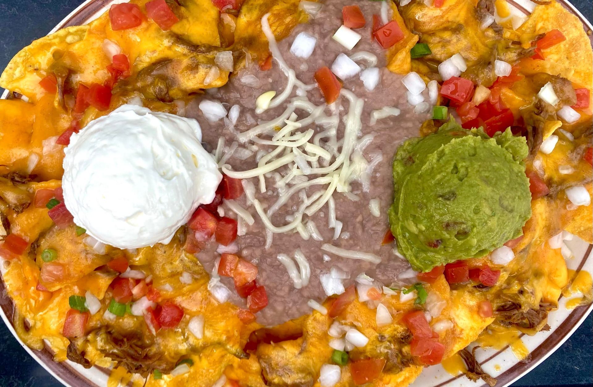 A plate of nachos with guacamole , sour cream and beans.
