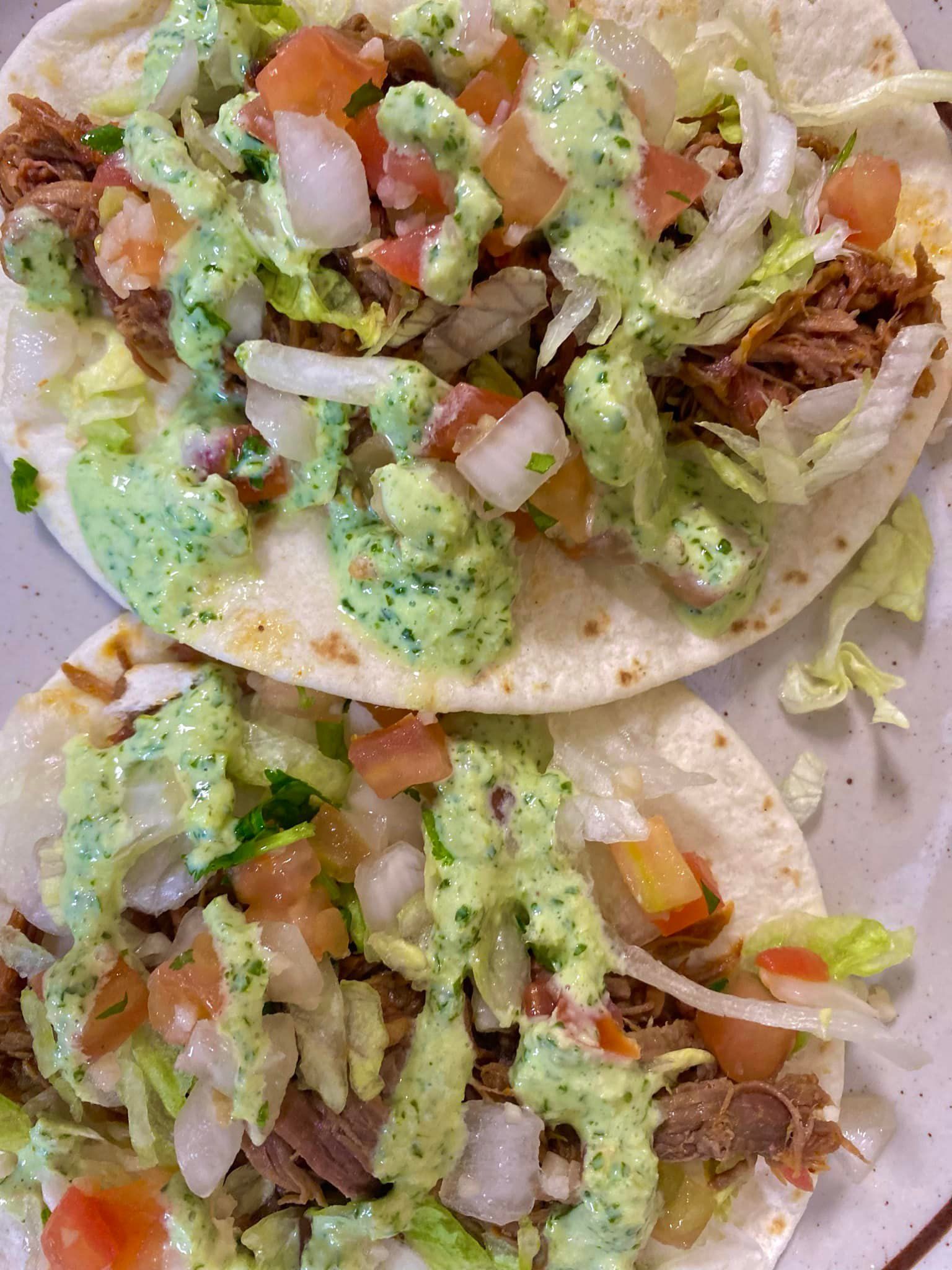 Two tacos with meat , lettuce , tomatoes and guacamole on a plate.