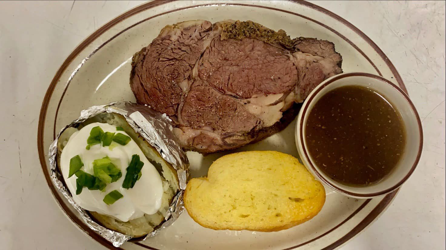 A plate of food with a steak , baked potato , cornbread and gravy.