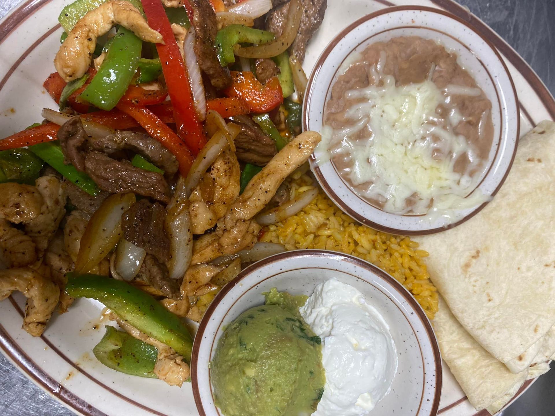 A plate of food with guacamole , beans , rice and a tortilla on a table.