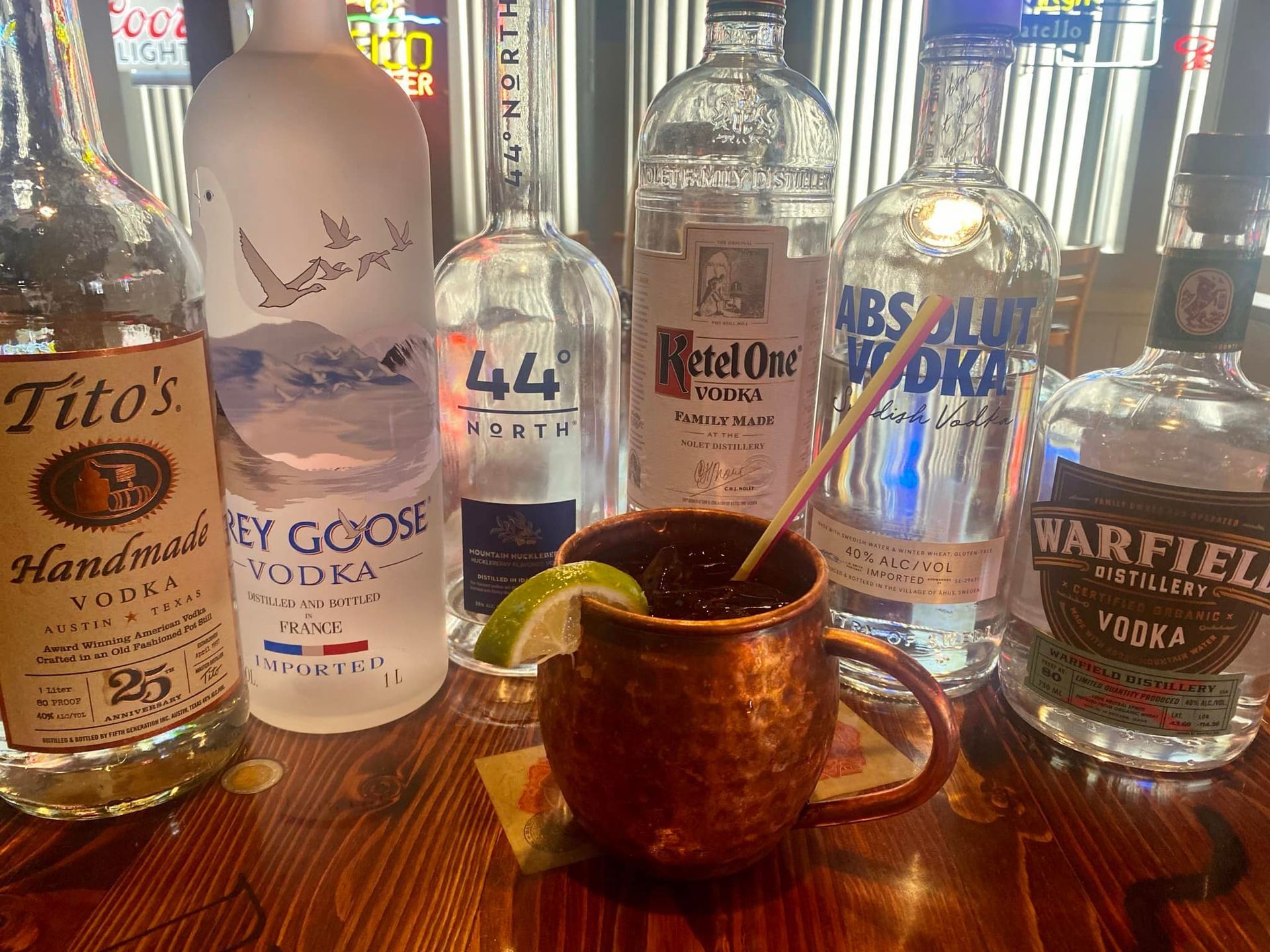 A bottle of tito 's vodka is sitting on a wooden table next to other bottles of vodka.