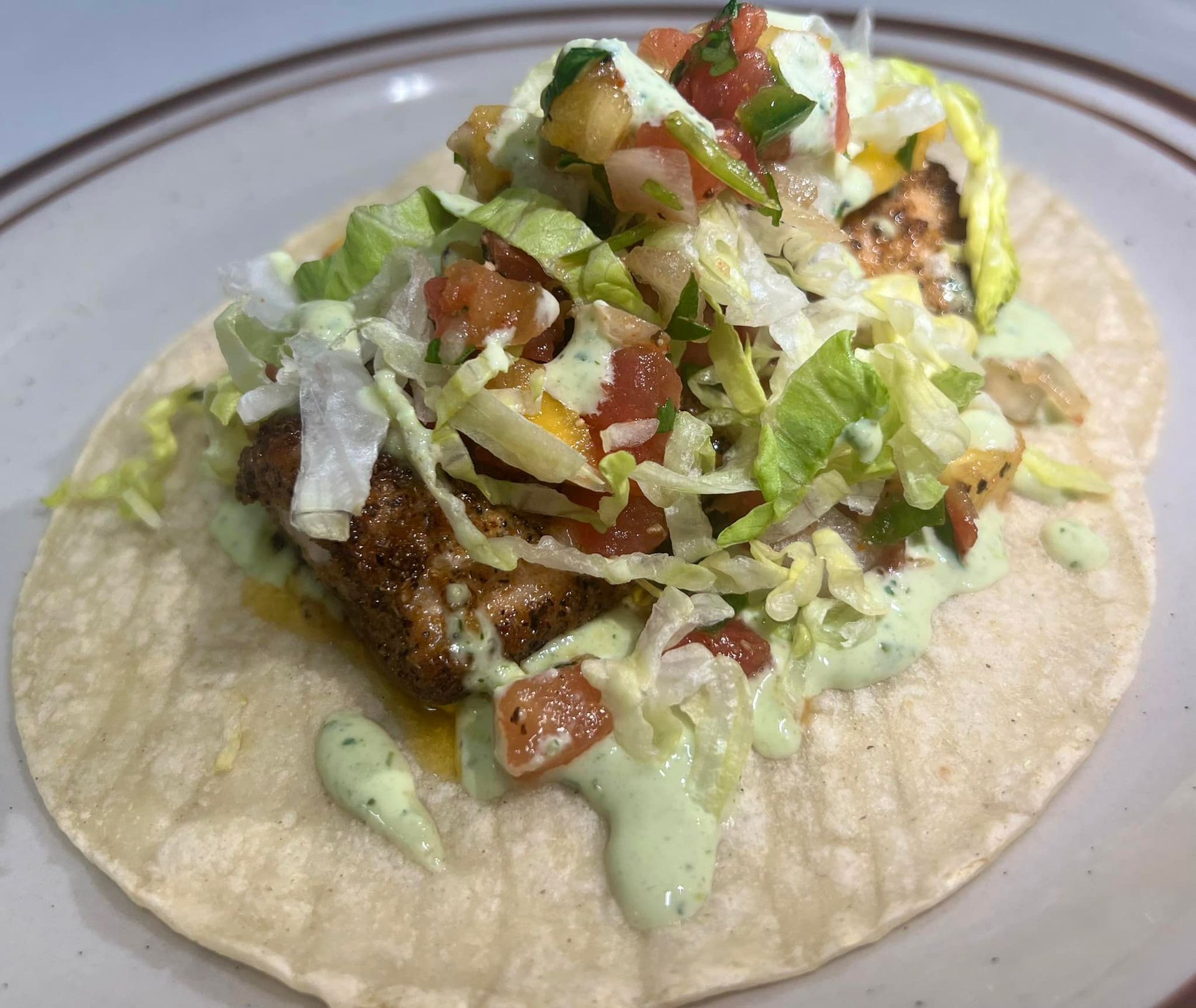 A taco with meat , lettuce , tomatoes and sauce on a plate.