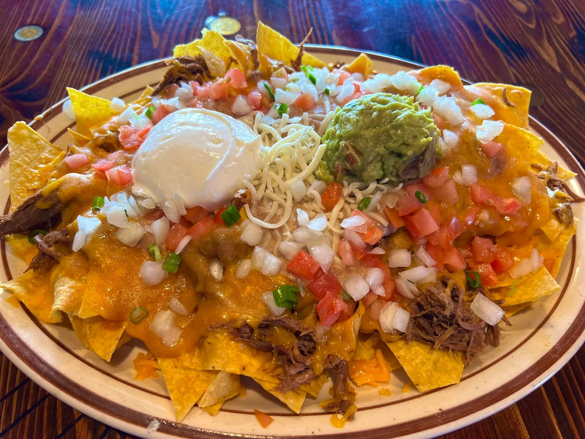 A plate of nachos with guacamole and sour cream on a wooden table.