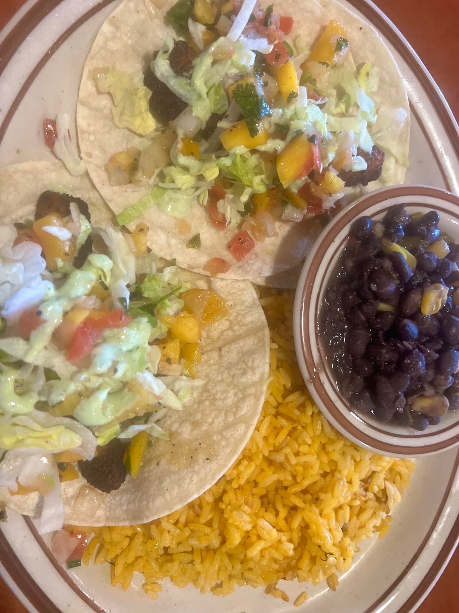 A plate of food with tacos , rice and beans on a table.