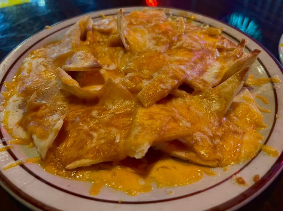 A close up of a plate of nachos with cheese on a table.
