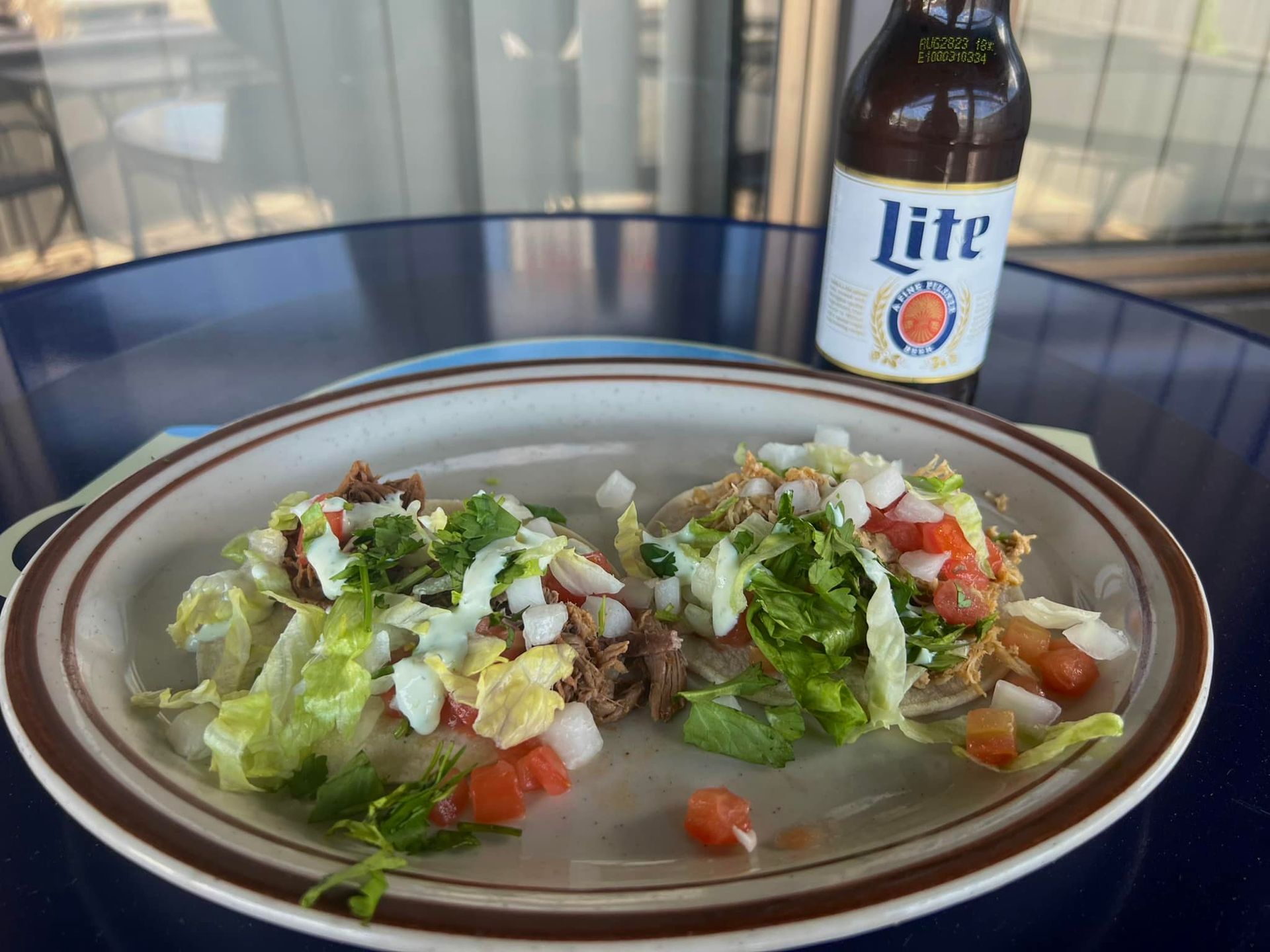 A plate of food and a bottle of lite beer on a table.