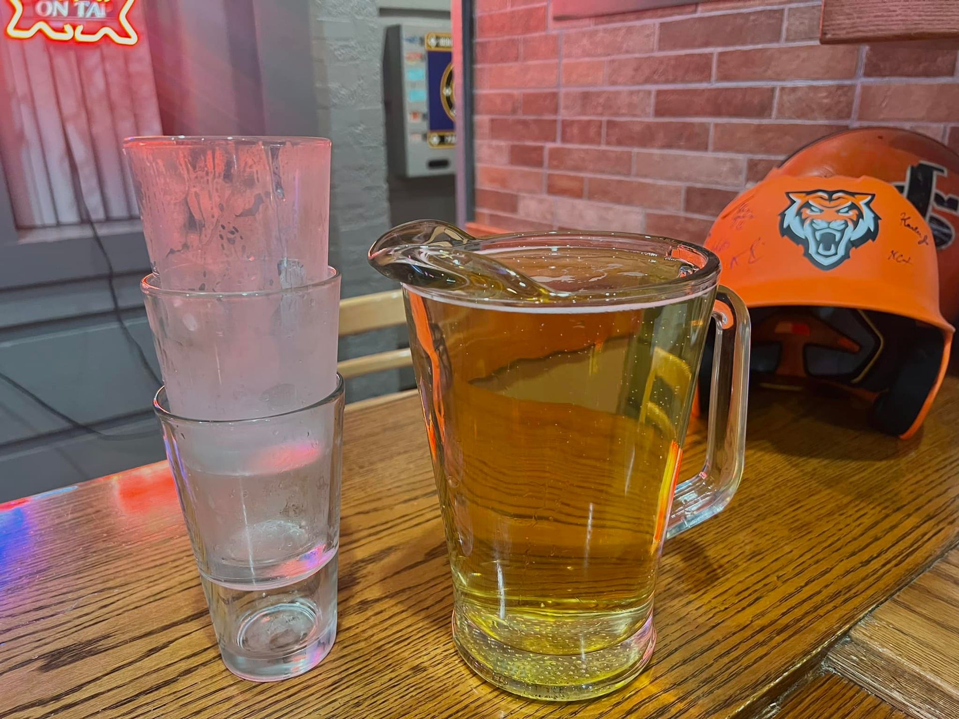 A pitcher of beer is sitting on a wooden table next to empty glasses.