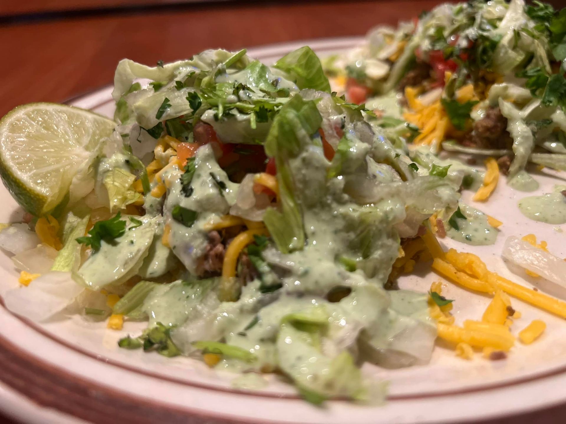 A close up of a plate of food with lettuce , cheese , tomatoes and lime wedges.