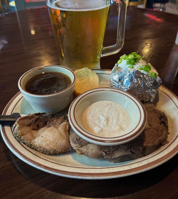 A plate of food on a table with a glass of beer in the background.