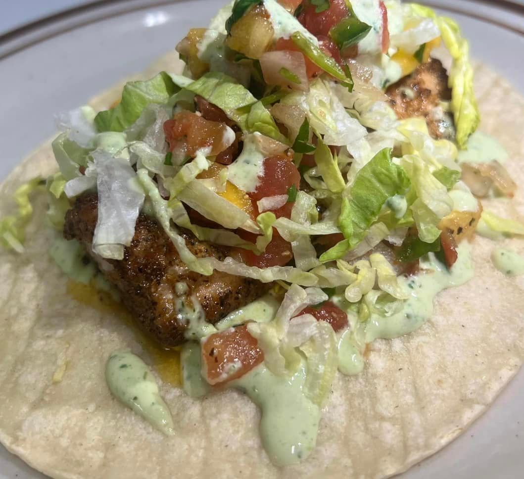 A taco with meat , lettuce , tomatoes and sauce on a plate.