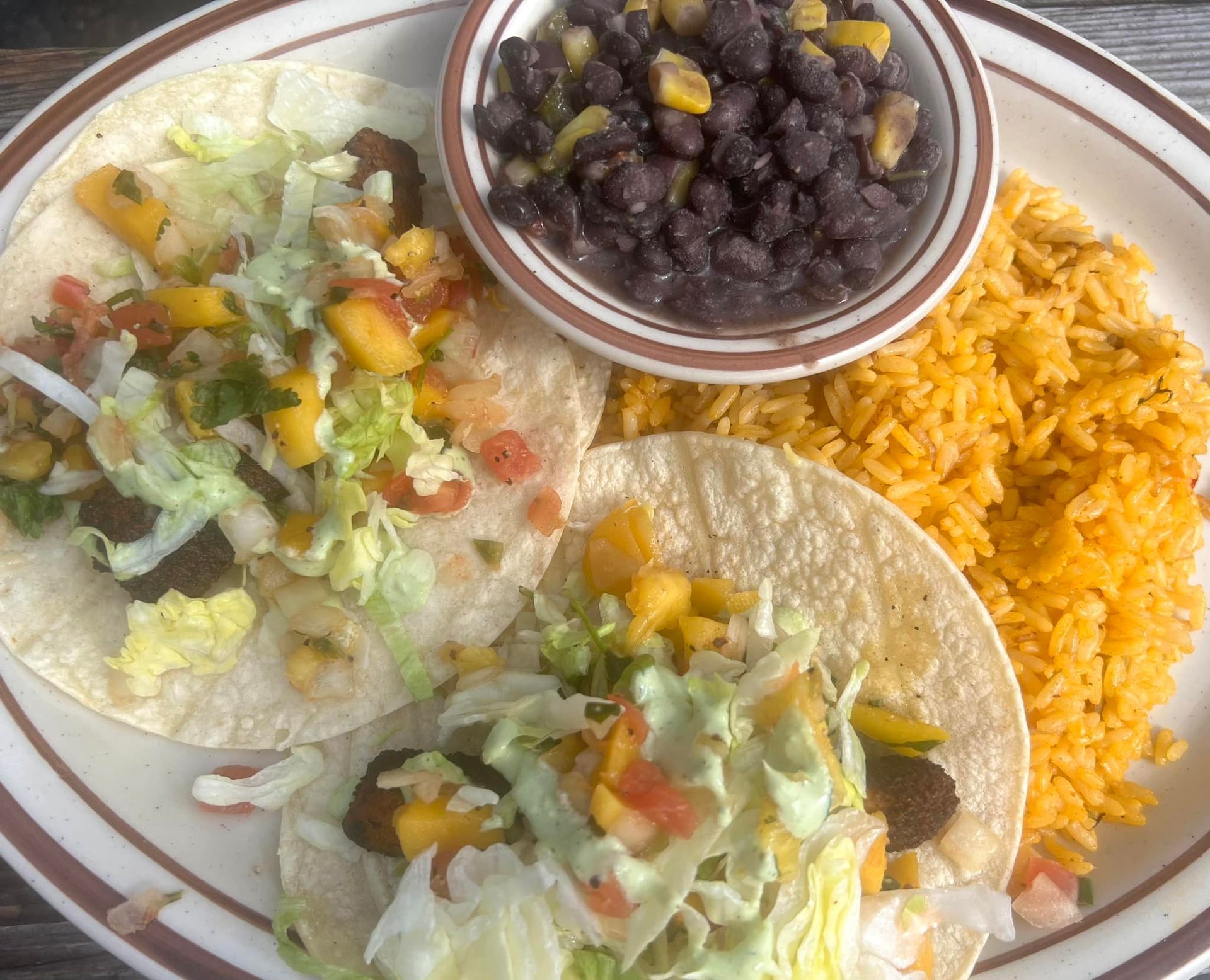 A plate of food with tacos , rice and beans on a table.