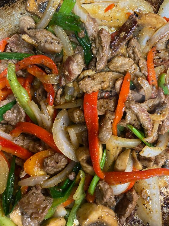 A close up of a plate of food with meat , peppers , onions and mushrooms.