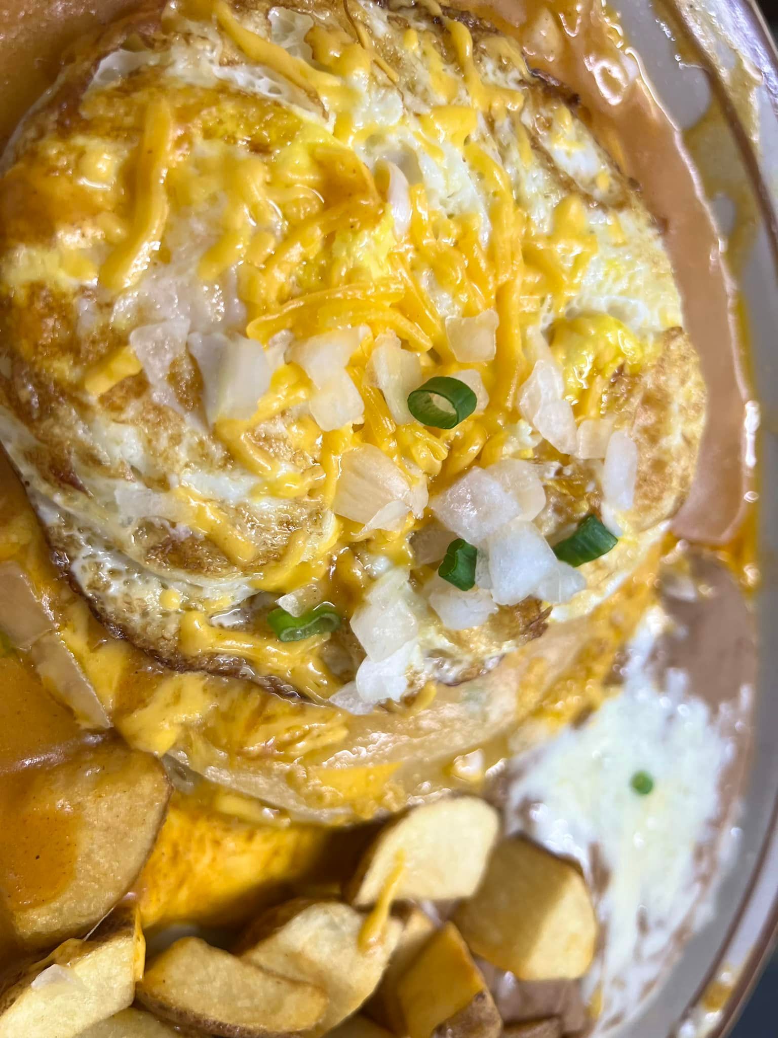 A close up of a plate of food with eggs , cheese , onions and potatoes.