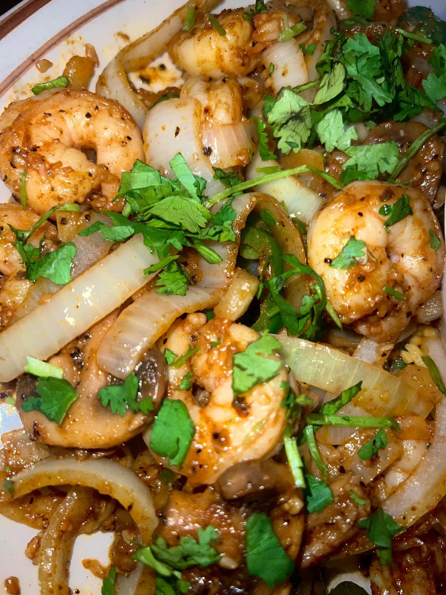 A close up of a plate of food with shrimp , mushrooms , onions and cilantro.