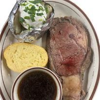 A plate of food with a roast beef , baked potato , bread and gravy.