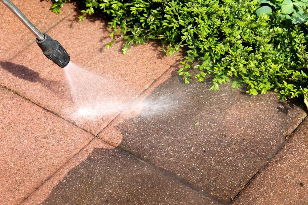 A person is using a high pressure washer to clean a brick walkway.