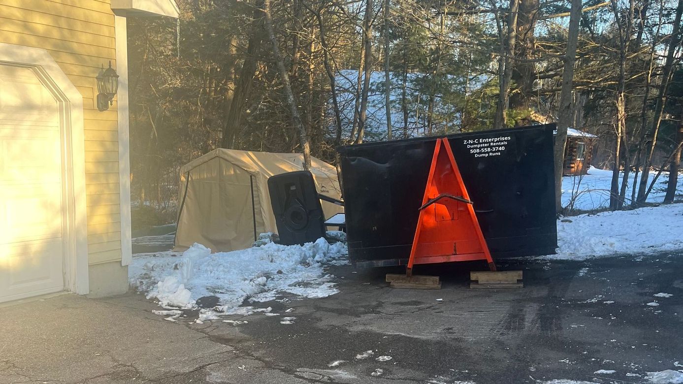 A black trash can is sitting in the snow in front of a garage.