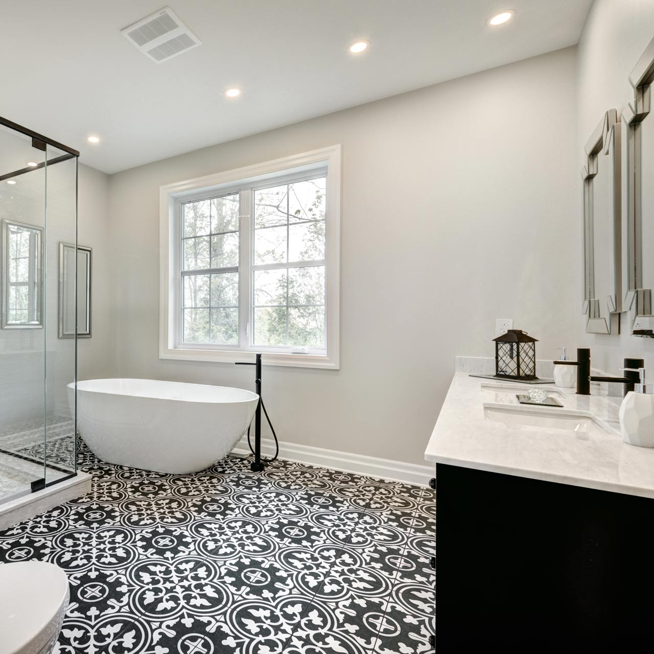Modern bathroom with a freestanding white tub, black patterned floor tiles, and a white vanity against light gray walls.