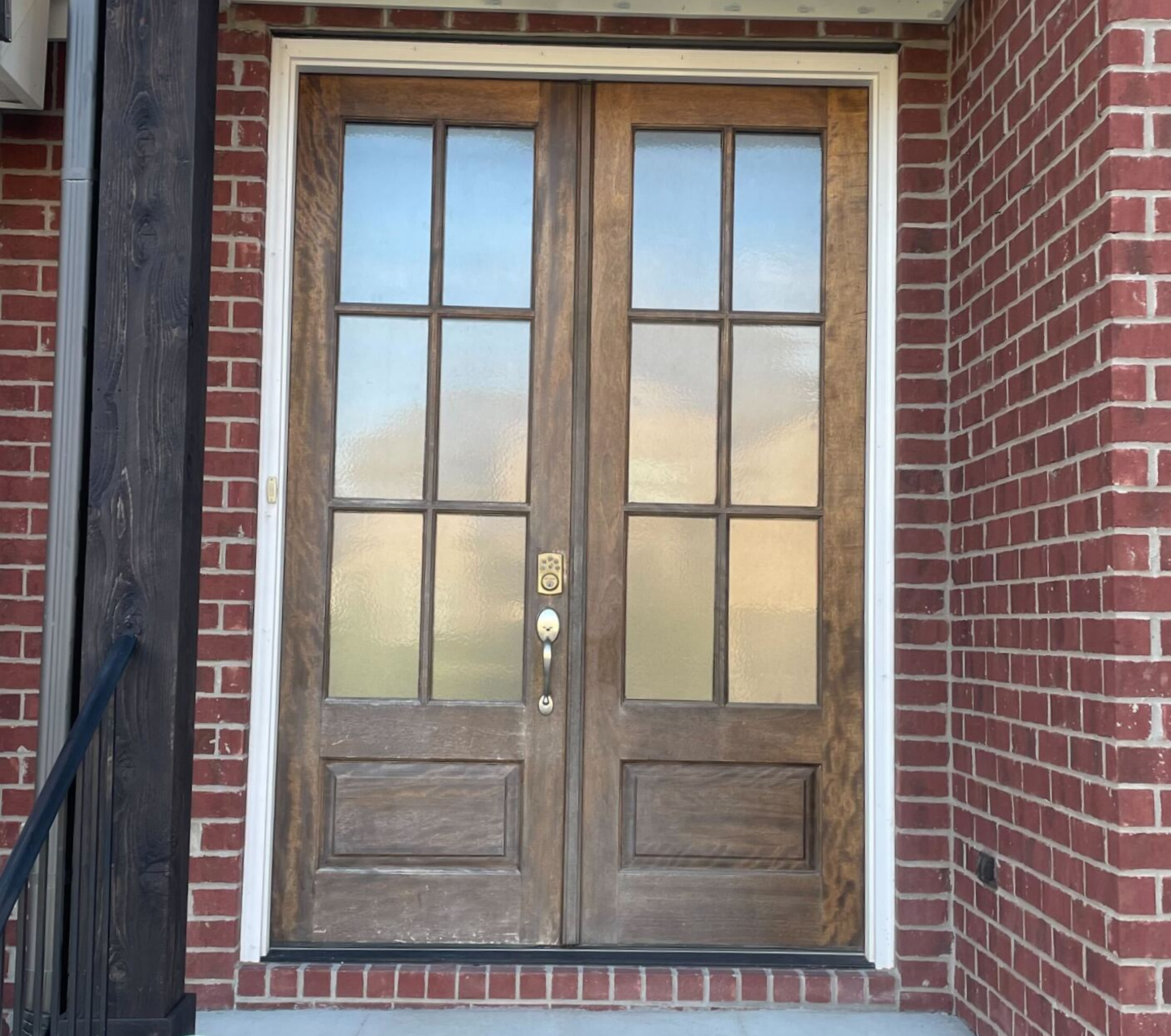 Wooden double front doors with glass panes, centered in a brick entryway