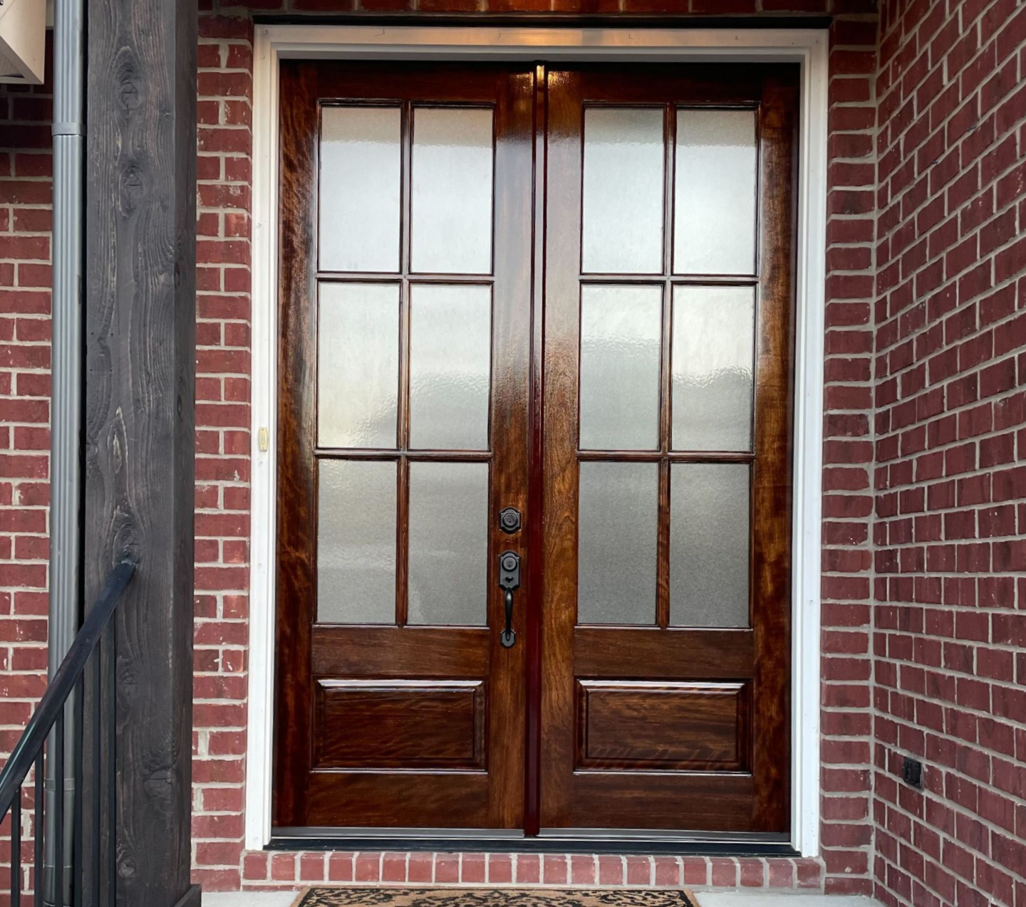 Wooden double front door with frosted glass panels set in a red brick entryway