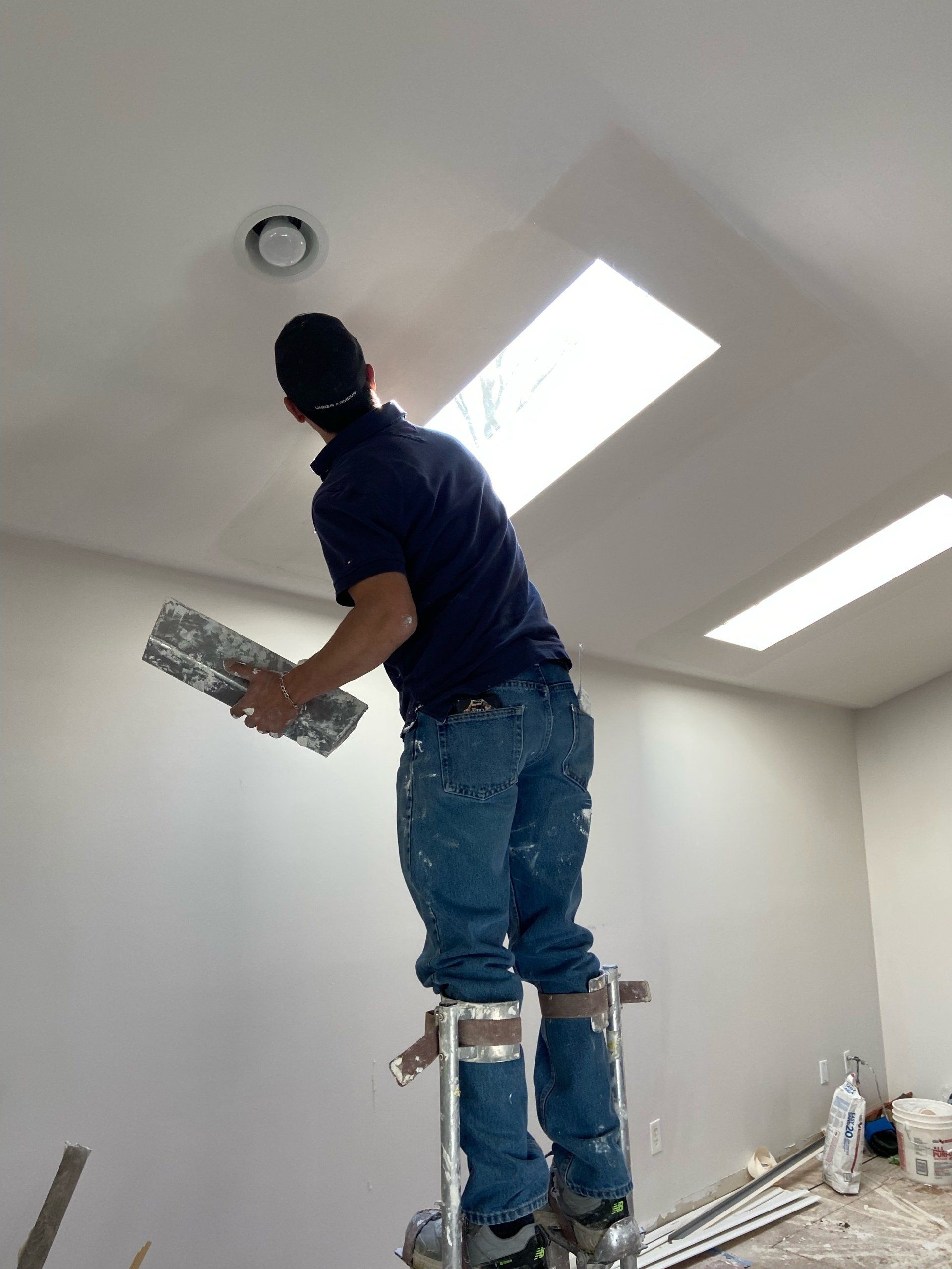 Worker on a ladder installing a ceiling light in a bright white room