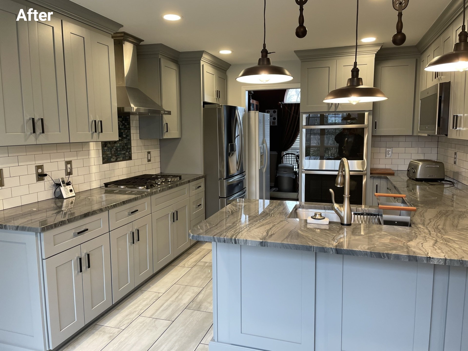 A renovated kitchen with light grey cabinets, granite countertops, stainless steel appliances, and pendant lighting.