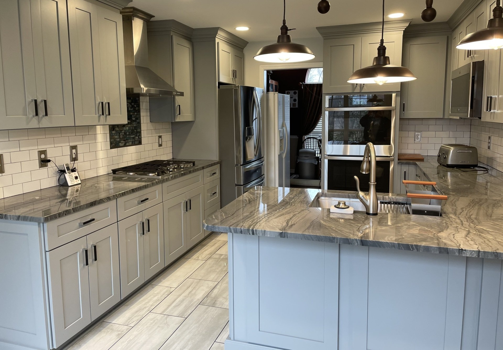 Modern kitchen with gray cabinets, marble island, pendant lights, and stainless steel appliances