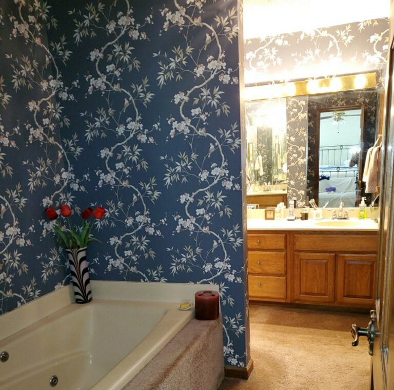 Blue floral bathroom with a corner tub, red flowers, and a vanity with mirror in an adjoining room