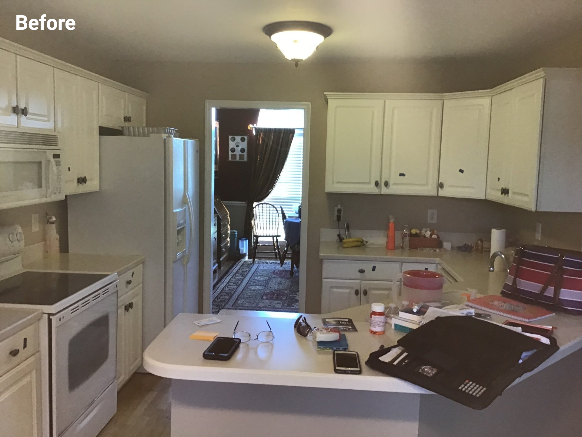 A kitchen with white cabinets, a white stove, a white refrigerator, and a cluttered counter viewed from a doorway.