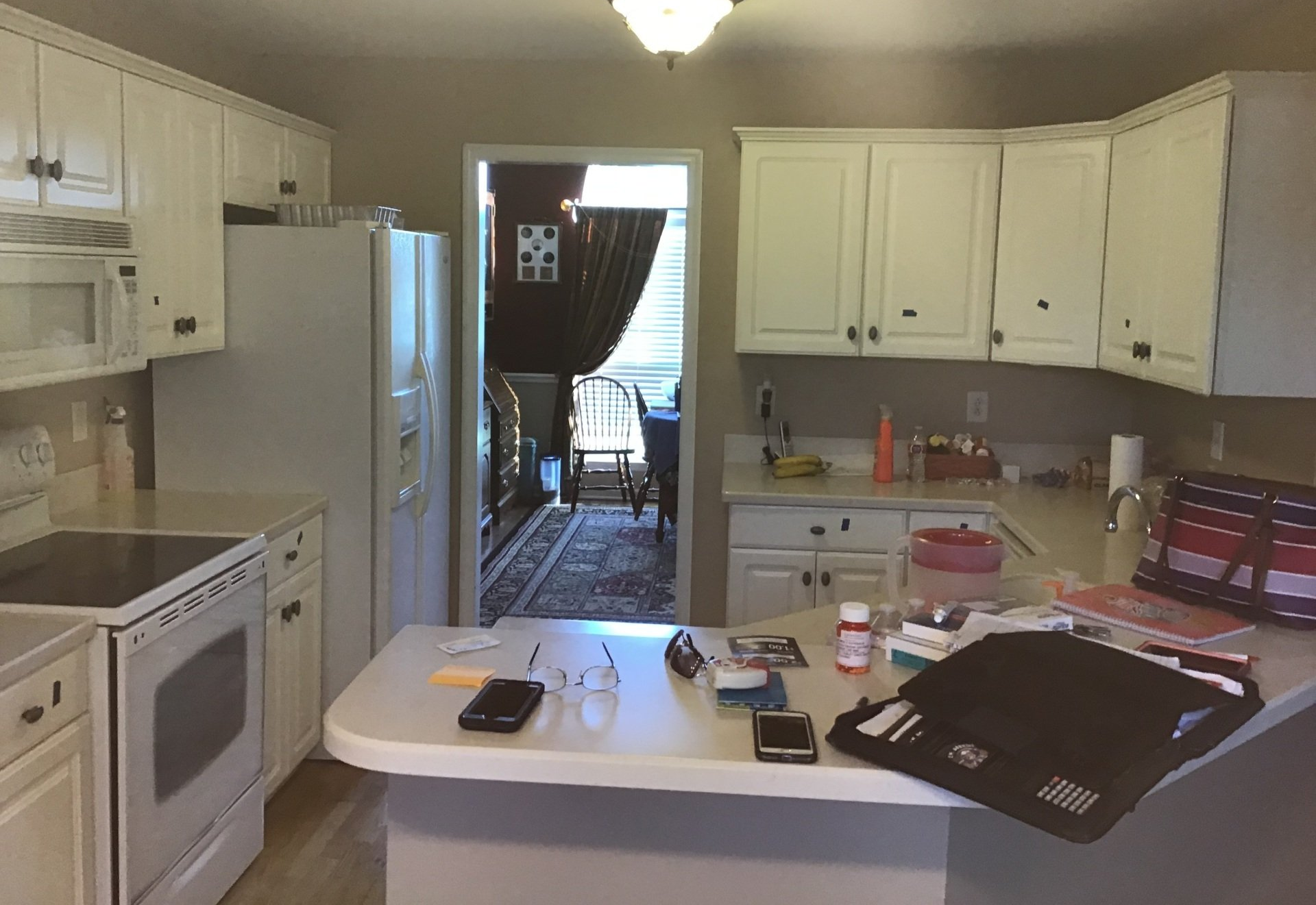 Kitchen interior with white cabinets, central island, and open doorway to a hallway beyond.
