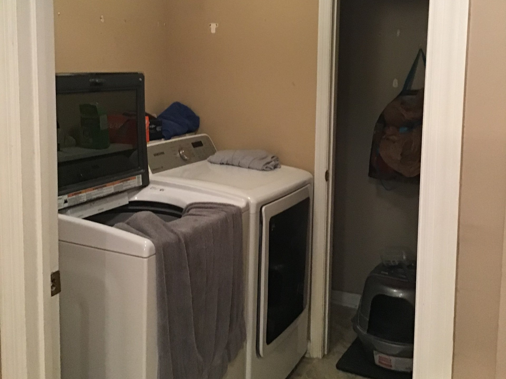 Small laundry room with two white appliances, a towel draped over one, and an open doorway.