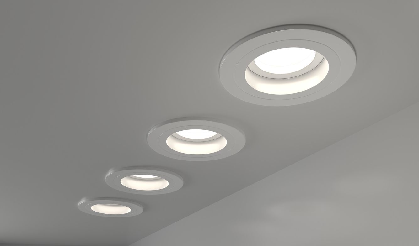Row of four recessed ceiling lights glowing in a white ceiling