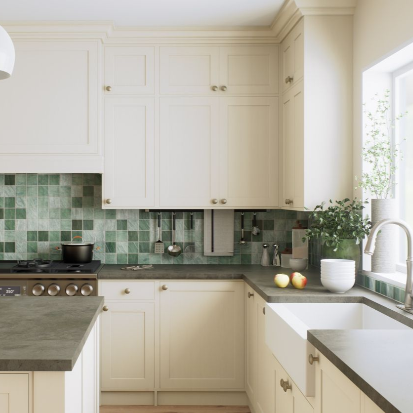 A kitchen with cream cabinets, a grey countertop, and a green, square-tiled backsplash featuring a farmhouse sink.