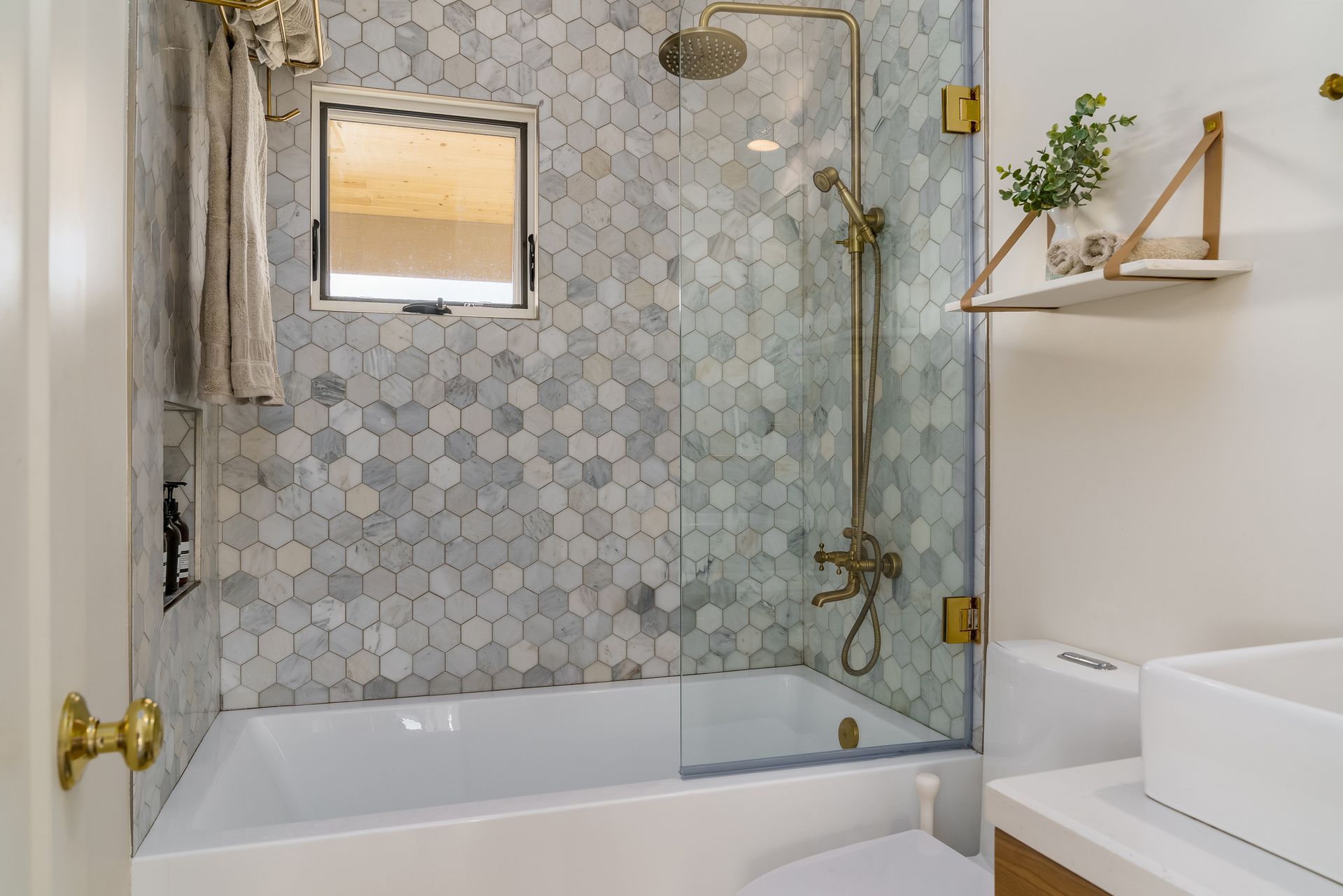 Modern bathroom with tiled shower, glass door, bathtub, and white sink area