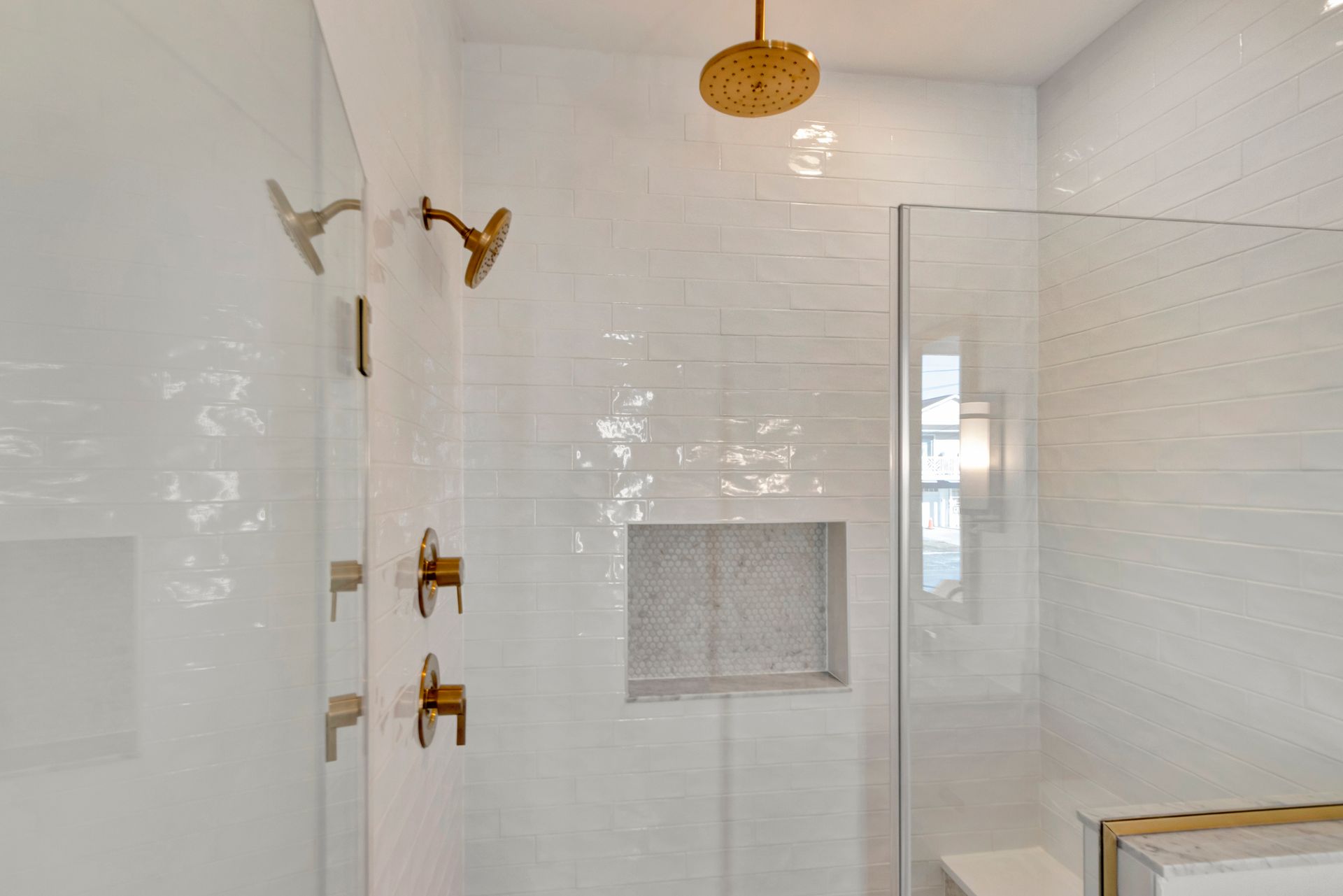 Modern white tiled shower with gold fixtures, glass door, and built-in niche.