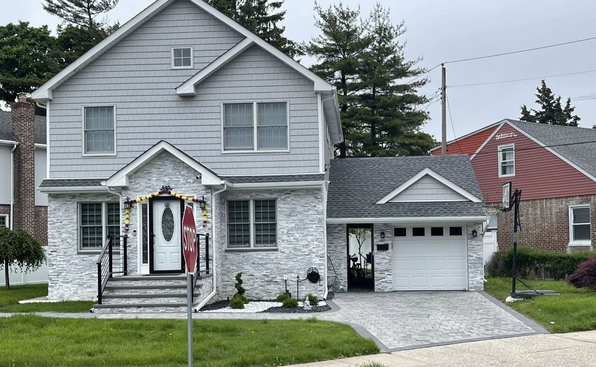 A large white house with a garage and a red house in the background.