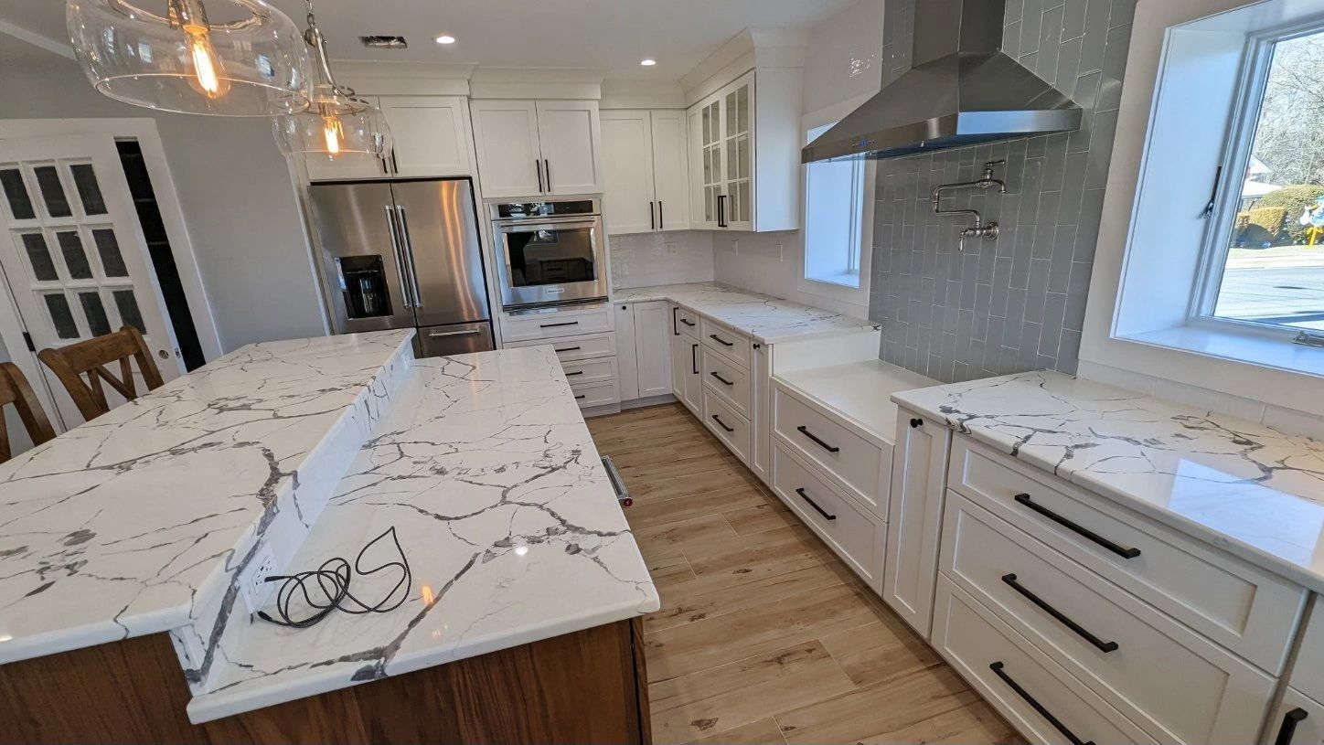 A kitchen with white cabinets , granite counter tops , stainless steel appliances and a large island.