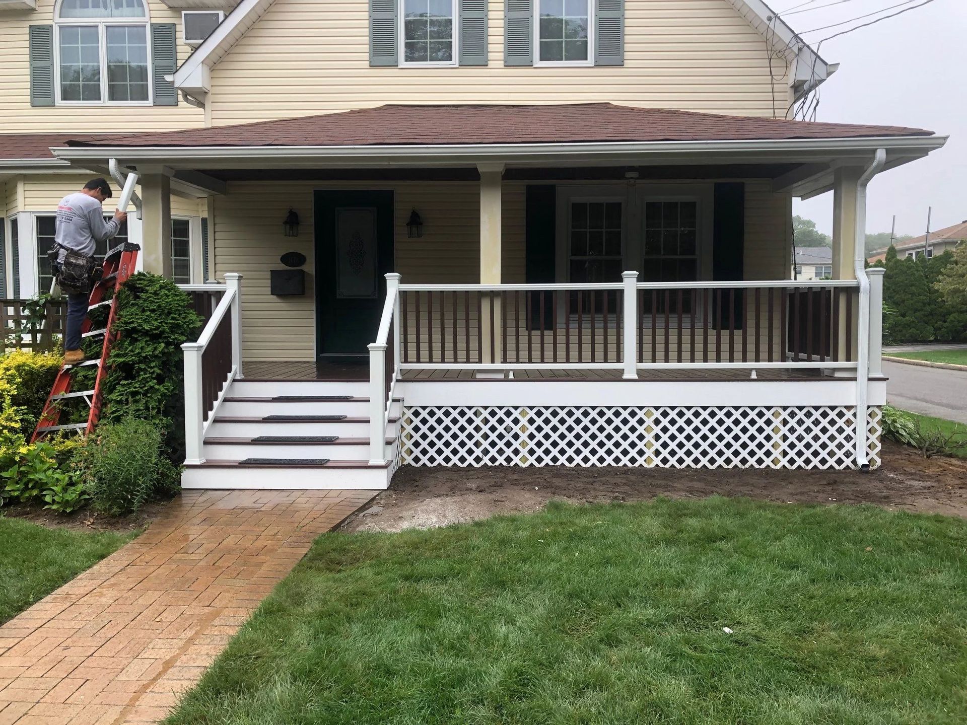 A man is standing on a ladder in front of a house with a porch.