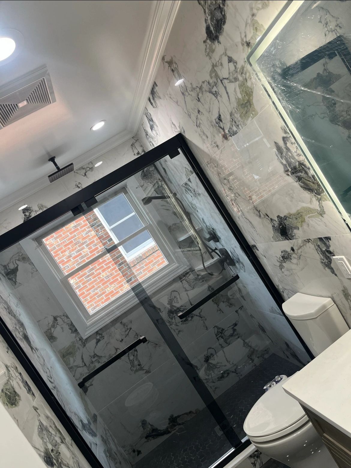 A bathroom with a toilet , sink , shower and window.